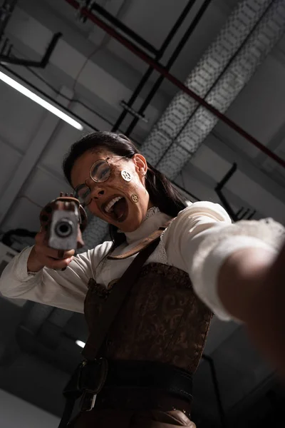 Foco seletivo de mulher steampunk irritado gritando e mirando com pistola na câmera — Fotografia de Stock
