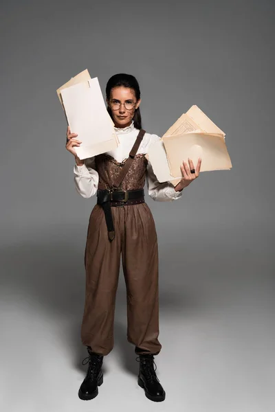 Full length view of steampunk woman in glasses holding documents on grey — Stock Photo