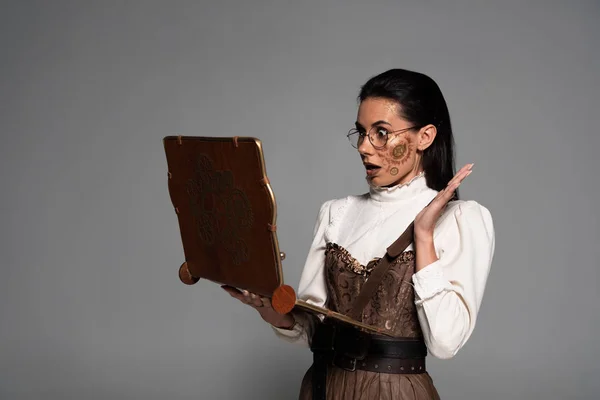 Ударная стимпанк-женщина в очках с помощью винтажного ноутбука, изолированного на сером — стоковое фото
