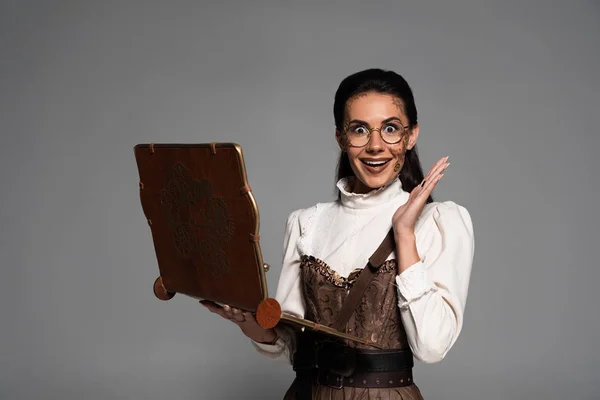 Excited steampunk woman in glasses using vintage laptop isolated on grey — Stock Photo