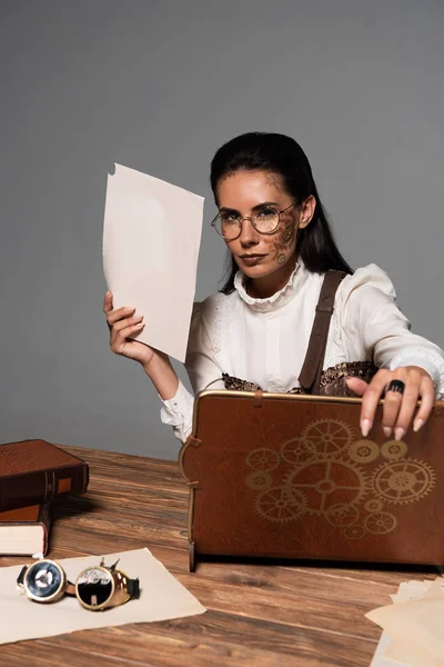 Steampunk donna in occhiali con documenti e laptop vintage sul posto di lavoro isolato su grigio — Foto stock