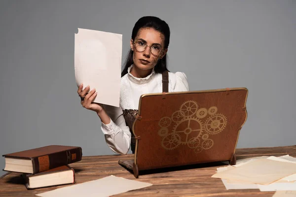 Стімпанк жінка в окулярах з документами і вінтажний ноутбук на робочому місці ізольована на сірому — стокове фото