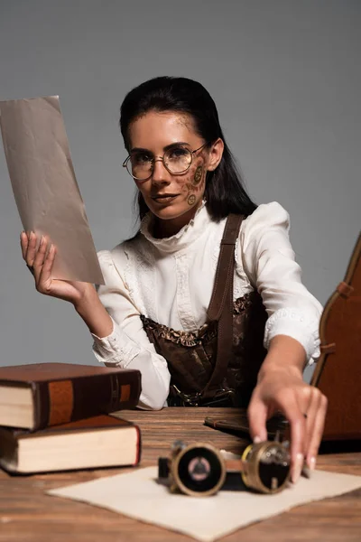 Стимпанк женщина держит документ и очки на рабочем месте изолированы на серый — стоковое фото