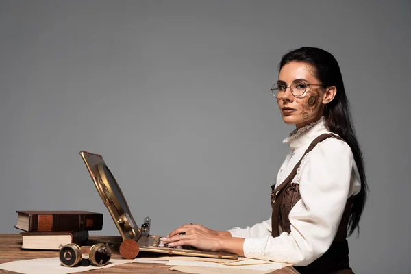 Mulher steampunk atraente usando laptop no local de trabalho isolado em cinza — Fotografia de Stock