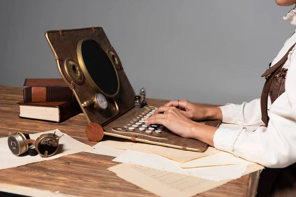 Cropped view of woman typing on steampunk laptop at table isolated on grey — Stock Photo