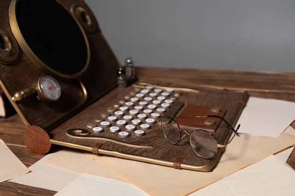 Portátil steampunk, gafas y documentos sobre mesa de madera aislada en gris - foto de stock