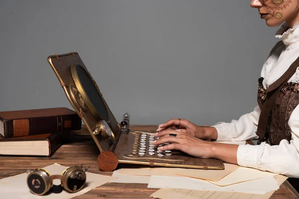 Vista recortada de la mujer escribiendo en el ordenador portátil steampunk en la mesa aislado en gris - foto de stock
