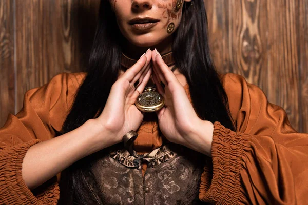 Vista cortada de mulher com maquiagem steampunk tocando medalhão em madeira — Fotografia de Stock