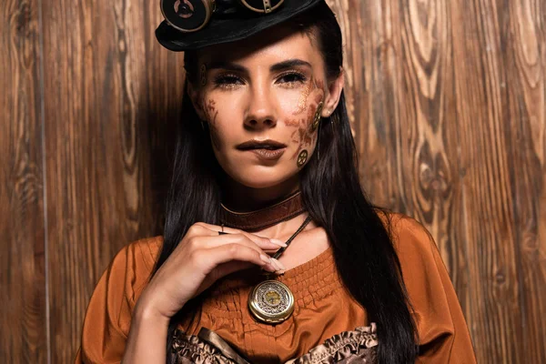 Attractive woman with steampunk makeup touching medallion on wooden — Stock Photo