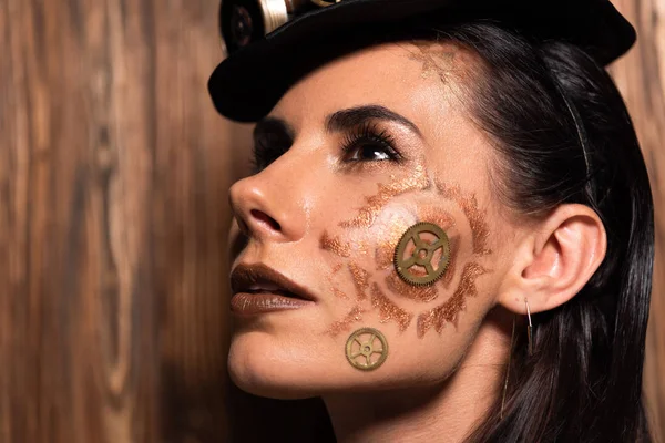 Mujer joven atractiva pensativa con maquillaje steampunk mirando hacia arriba en madera - foto de stock