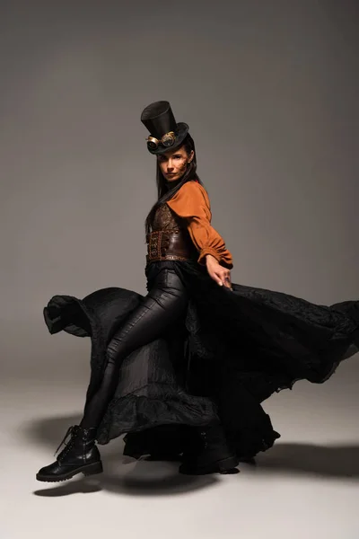 Full length view of attractive steampunk woman in top hat with goggles on grey — Stock Photo