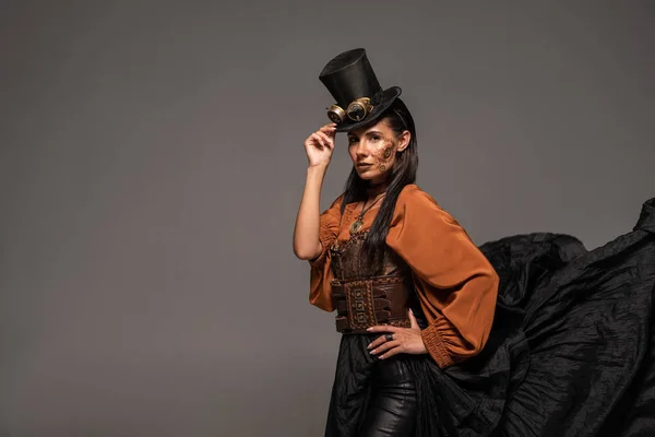 Стемпанк-женщина в верхней шляпе с когтями, стоящая с рукой на бедре, изолированная от серого — стоковое фото