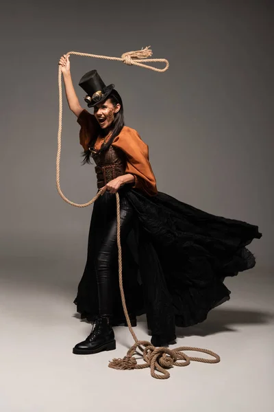 Full length view of beautiful screaming steampunk woman holding lasso on grey — Stock Photo