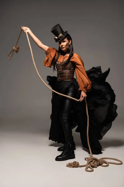 Full length view of beautiful steampunk woman holding lasso on grey — Stock Photo