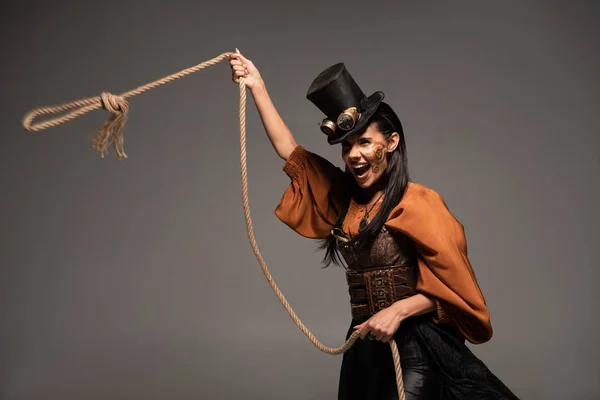 Atractiva chica steampunk en sombrero de copa sosteniendo lasso y gritando aislado en gris - foto de stock