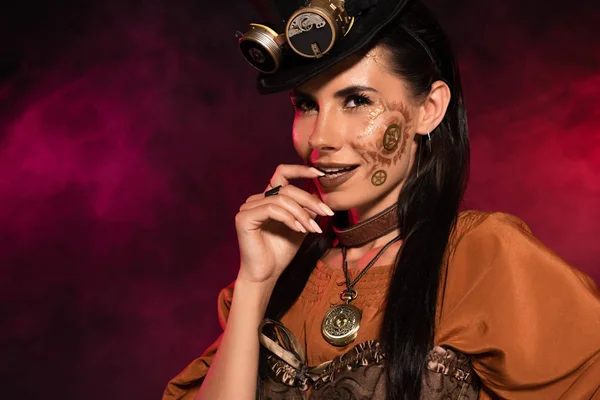 Attractive steampunk woman smiling and biting finger in pink smoke — Stock Photo