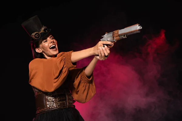 Schöne Steampunk-Frau mit Zylinder hält Pistole in der Hand und schreit in rosa Rauch auf schwarz — Stockfoto