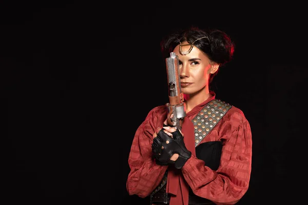 Confident steampunk young woman holding pistol isolated on black — Stock Photo