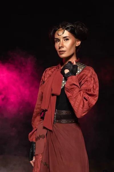 Attractive steampunk woman looking at camera in smoke on black — Stock Photo