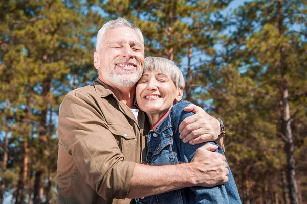 Sorridente coppia di turisti anziani che abbracciano con gli occhi chiusi nella giornata di sole — Foto stock