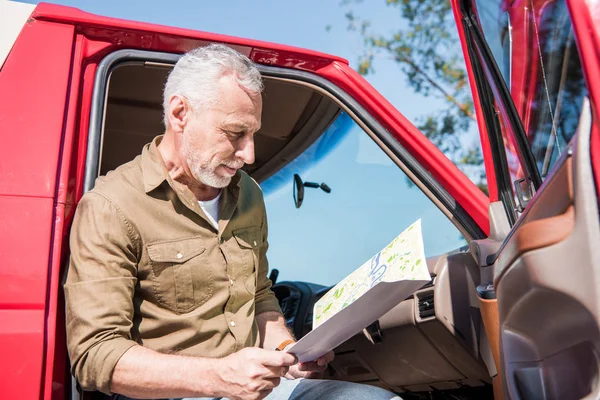 Senior traveler sitting in car and holding map in sunny day — Stock Photo