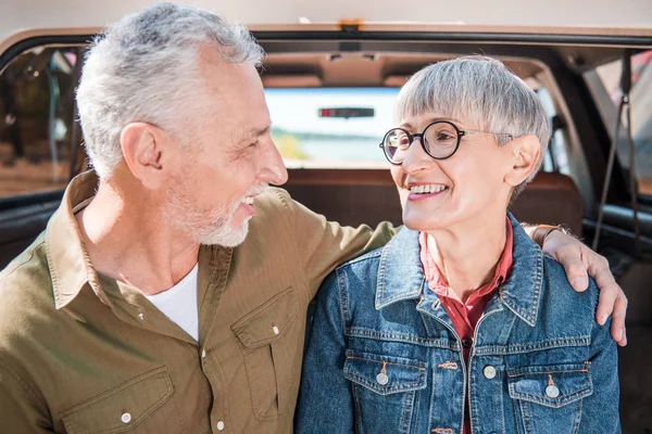 Smiling senior couple embracing and looking at each other near car — Stock Photo