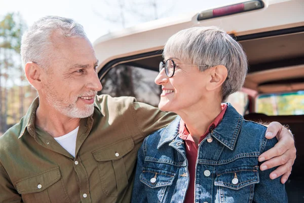 Lächelndes Senioren-Paar umarmt sich und blickt sich in der Nähe des Autos an — Stockfoto