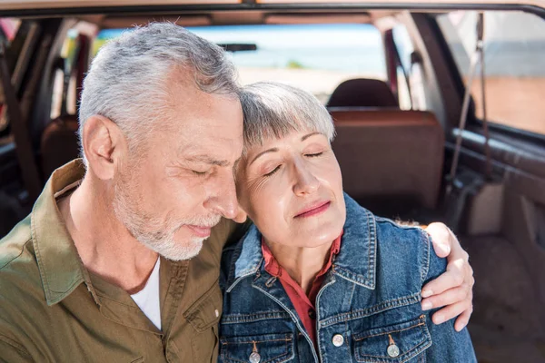 Pareja mayor abrazando con los ojos cerrados cerca del coche - foto de stock