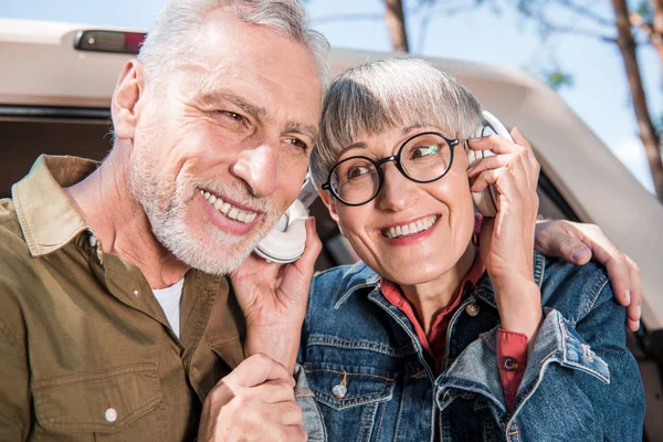 Smiling senior couple of tourists listening music in headphones — Stock Photo