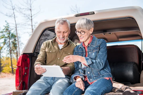 Smiling senior couple sitting in car and using digital tablet in sunny day — Stock Photo