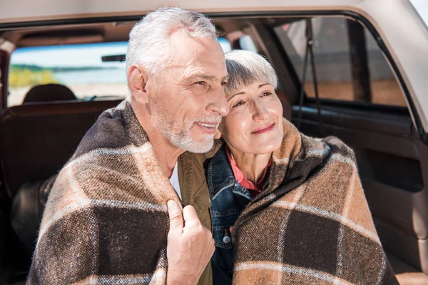 Smiling senior couple sitting in car with blanket — Stock Photo