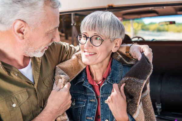 Smiling senior couple sitting in car with blanket and looking at each other — Stock Photo