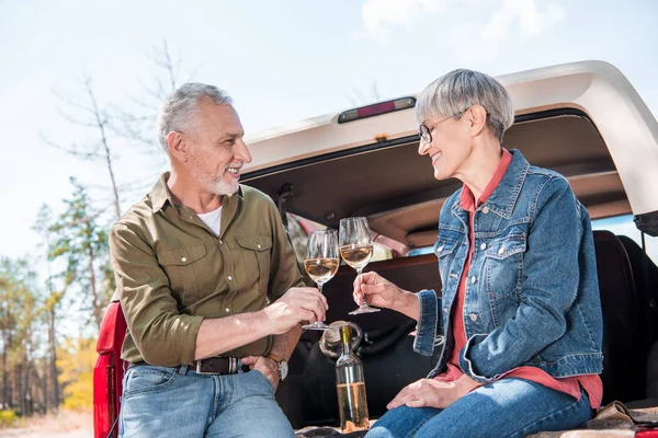 Happy senior couple clinking wine glasses and looking at each other near car — Stock Photo
