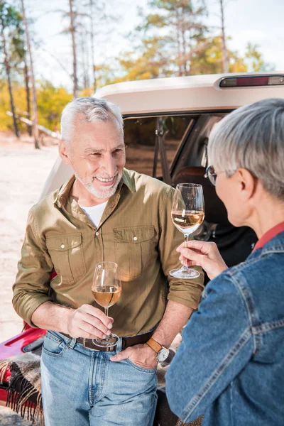 Heureux couple âgé debout près de la voiture avec des verres à vin et en se regardant — Photo de stock