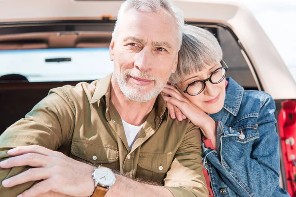 Happy senior couple standing together near car in sunny day — Stock Photo