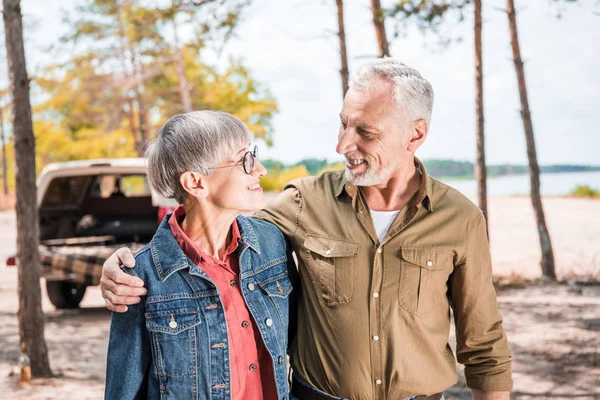 Happy senior couple embracing and looking at each other in forest in sunny day — Stock Photo