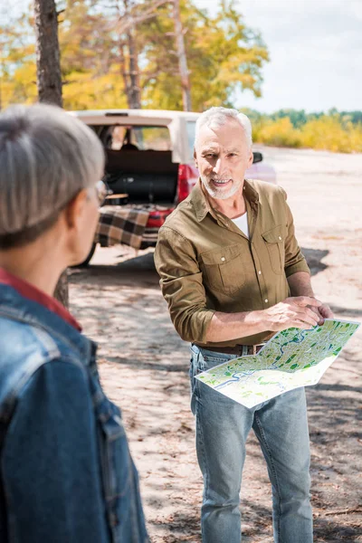 Foyer sélectif de couple de personnes âgées avec carte près de la voiture dans la forêt par temps ensoleillé — Photo de stock