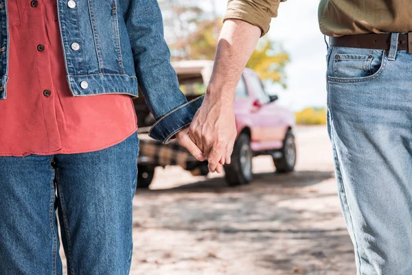Cropped view of senior couple holding hands near car in forest — Stock Photo