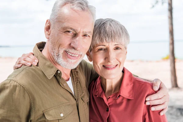 Feliz pareja de ancianos abrazando y sonriendo en la playa - foto de stock
