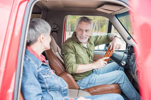 Seniorenpaar schaut sich lächelnd im Auto an — Stockfoto