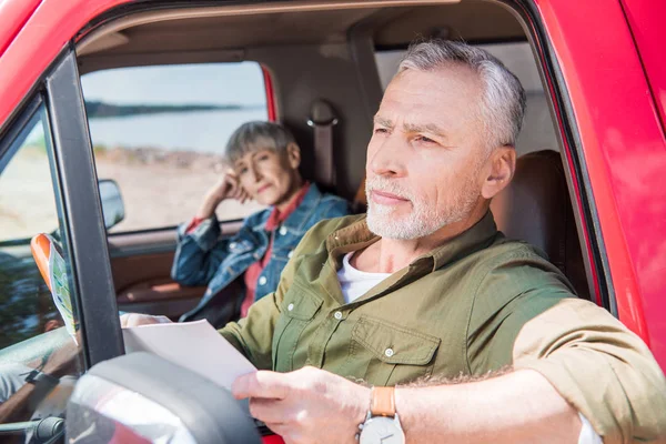 Hombre mayor sosteniendo mapa mientras está sentado en el coche con su esposa - foto de stock