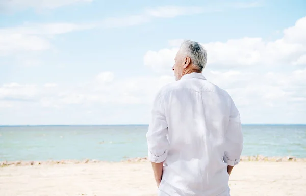 Вид сзади пожилого человека в белой рубашке на пляже в солнечный день — стоковое фото