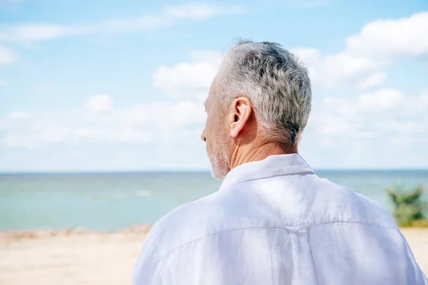 Вид ззаду на старшого чоловіка в білій сорочці на пляжі в сонячний день — стокове фото