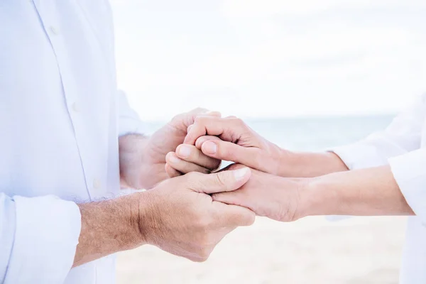 Vista recortada de pareja mayor en camisas blancas cogidas de la mano bajo el cielo azul - foto de stock