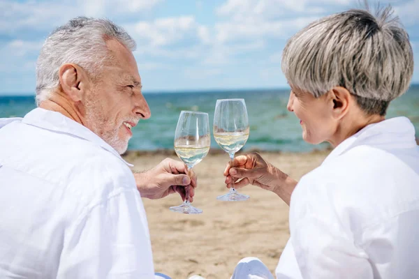 Smiling senior couple holding wine glasses with wine and looking at each other at beach — Stock Photo