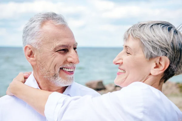 Sonriente pareja de ancianos abrazándose y mirándose cerca del río - foto de stock