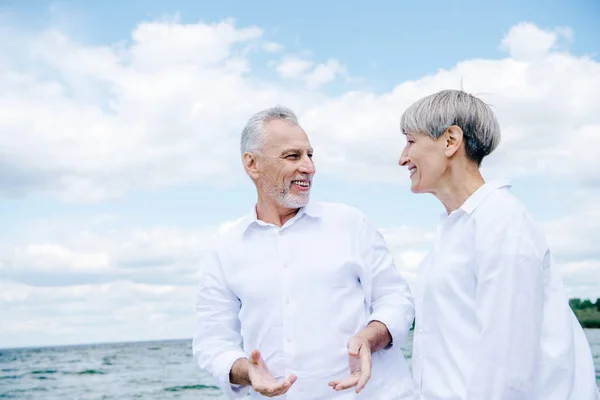 Feliz sonriente pareja de ancianos en camisas blancas mirándose bajo el cielo azul - foto de stock