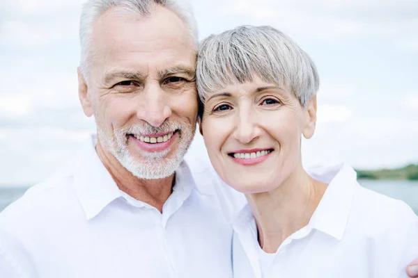 Вид улыбающейся счастливой пожилой пары в белых рубашках, смотрящей в камеру — стоковое фото