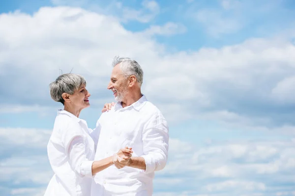 Счастливая старшая пара смотрит друг на друга, танцуя под голубым небом — стоковое фото