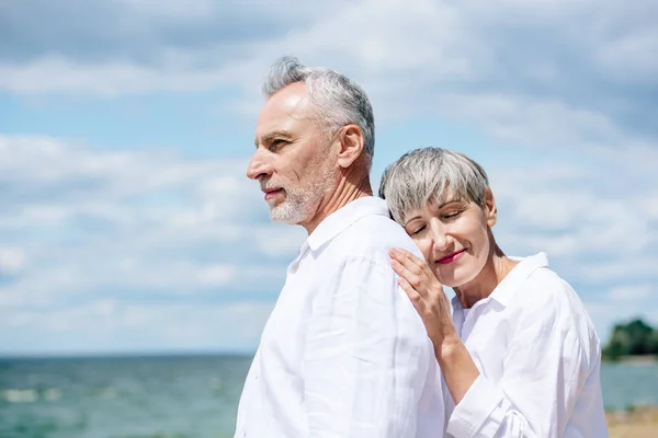 Feliz casal sênior em camisas brancas de pé sob o céu azul no dia ensolarado — Fotografia de Stock